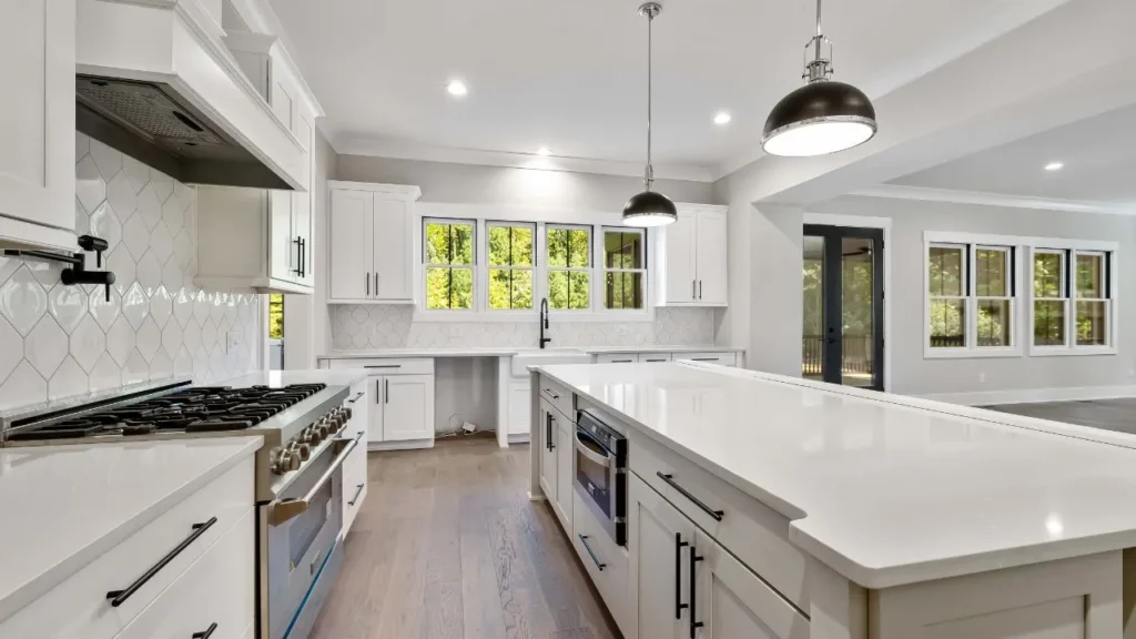 Spacious modern interior featuring freshly repainted white kitchen cabinets, a large quartz island, and matte black dome pendant lights