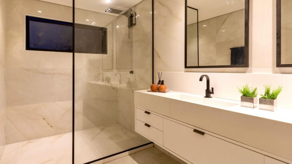 A curated selection of modern bathroom decorations featuring a marble tray, amber glass soap dispenser, and a small houseplant on a white vanity.