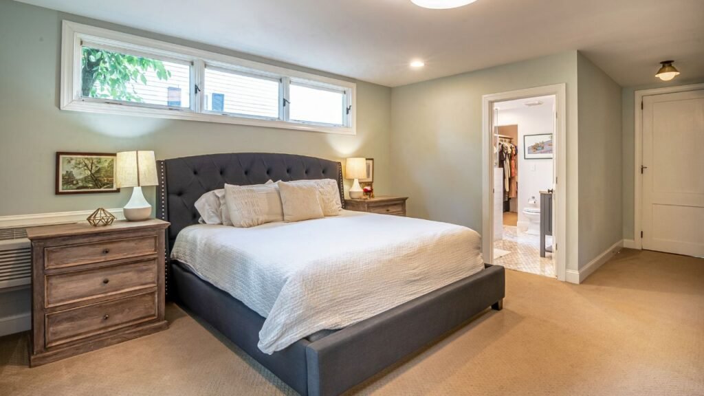 A stylish room highlighting an average bedroom size, efficiently utilizing the floor plan with a slatted wood accent wall, a glass en-suite bathroom, and a large sliding wardrobe.