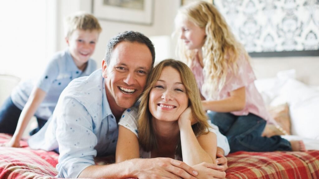 A happy family of four smiling and relaxing together in their el dormitorio, which translates to bedroom in spanish, creating a warm and inviting household atmosphere.