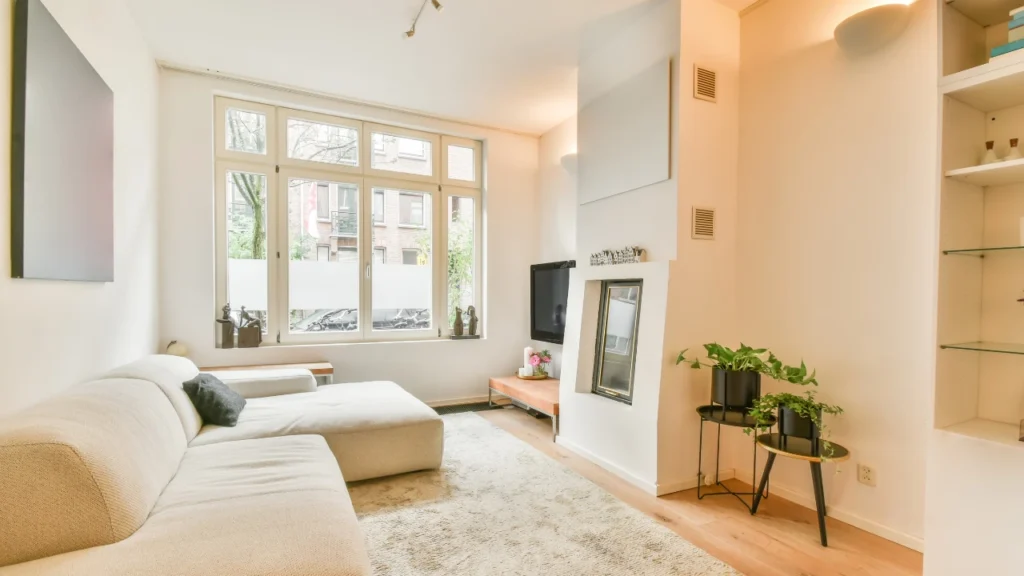 Bright, modern living room with a beige sofa, fireplace, TV, and large window