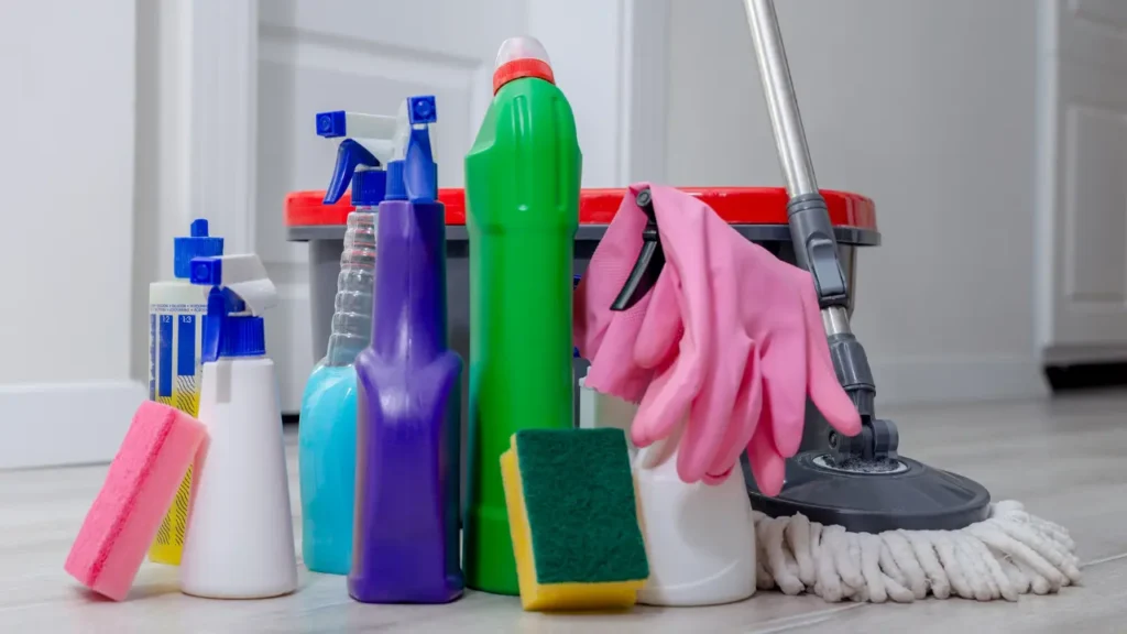 Assortment of cleaning supplies including sponges, spray bottles, pink gloves, and a mop