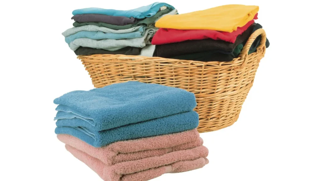 Wicker laundry basket filled with folded colorful t-shirts next to stacked blue and pink towels