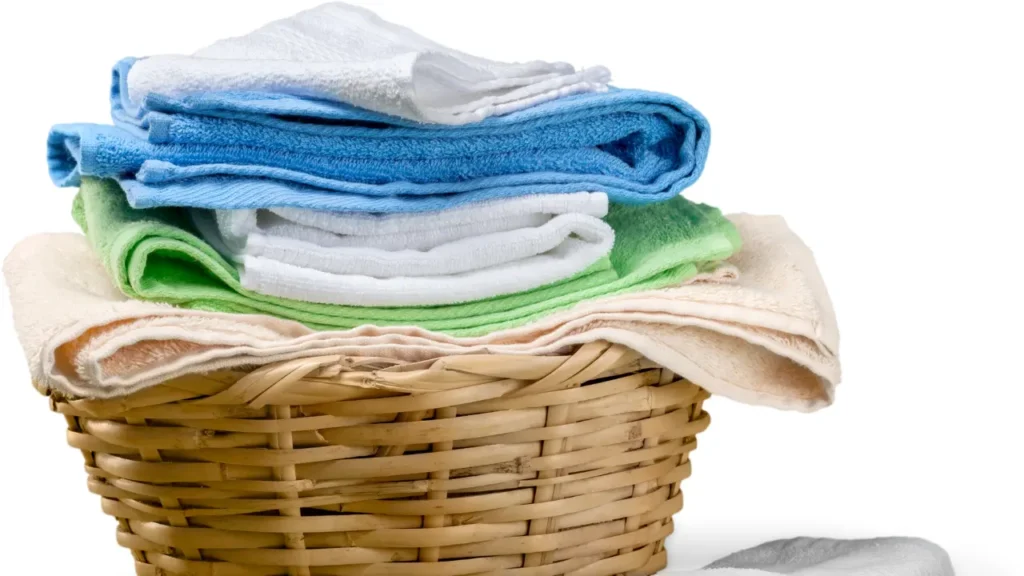 Neatly folded blue, white, and green towels piled on top of a woven wicker laundry basket