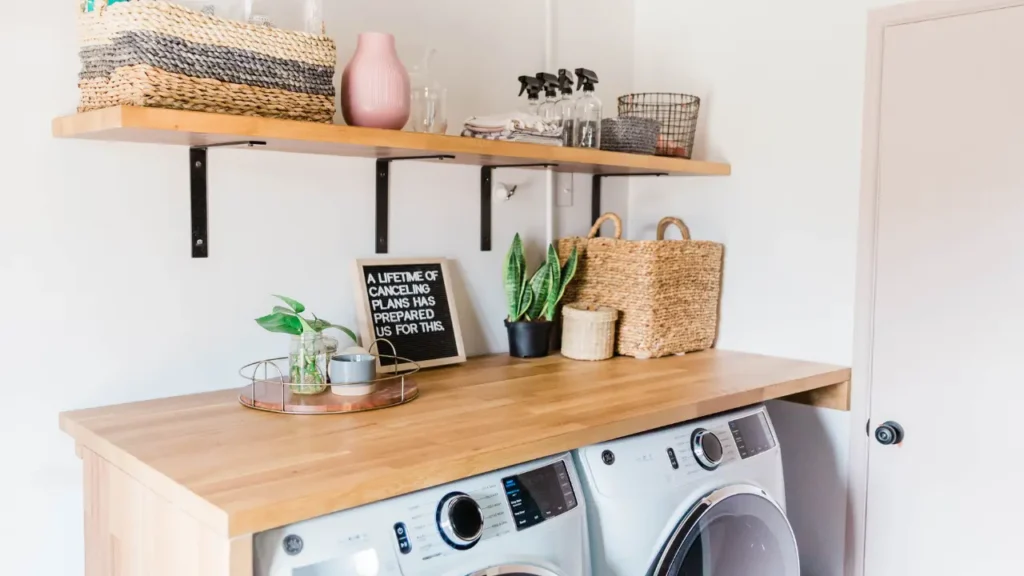 Stylish laundry room with open shelving, woven baskets, plants, and a humorous sign above a washer and dryer