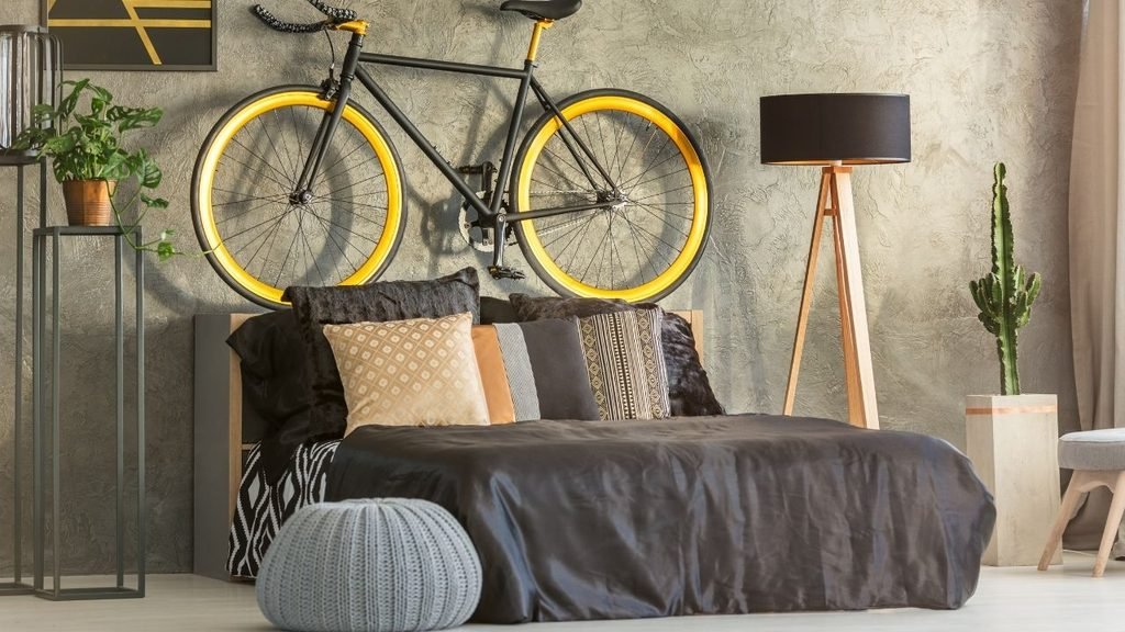 Industrial-style bedroom with a black and yellow bicycle mounted on a textured wall above a dark upholstered bed