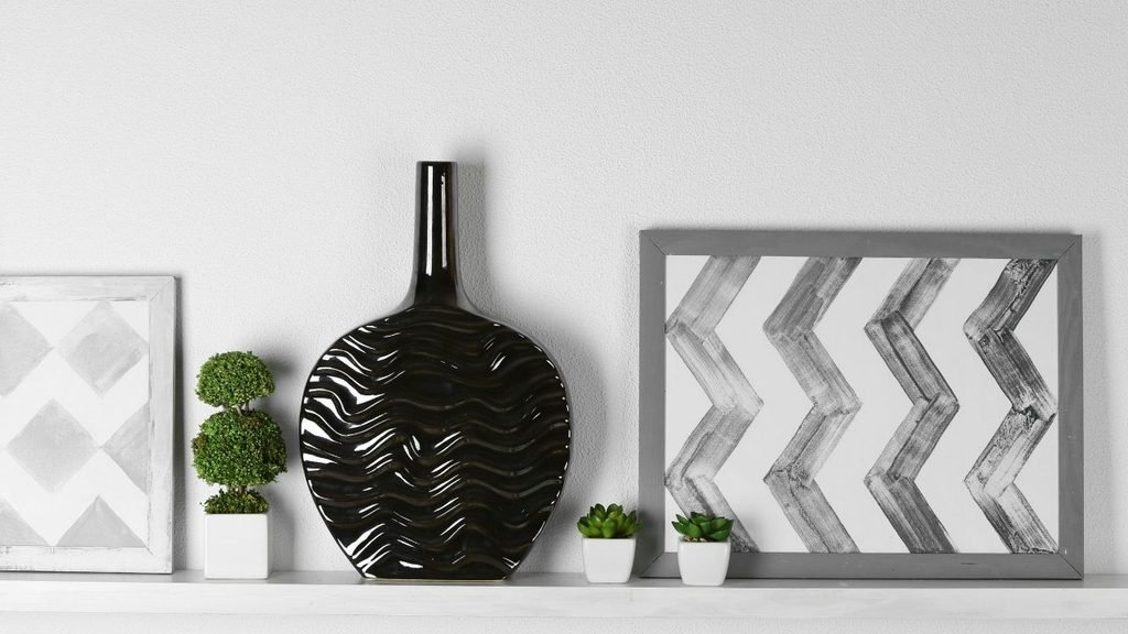 Decorative shelf styling with a black wave-patterned vase, framed geometric prints, and small succulents
