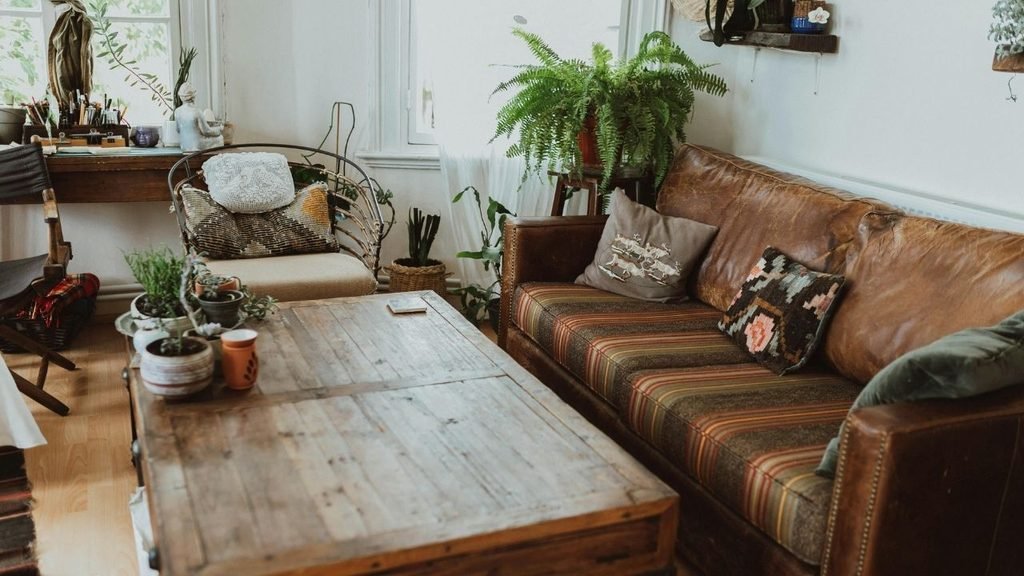 Bohemian living room with a tan leather sofa, striped cushions, a reclaimed wood coffee table, and potted ferns by a bright window