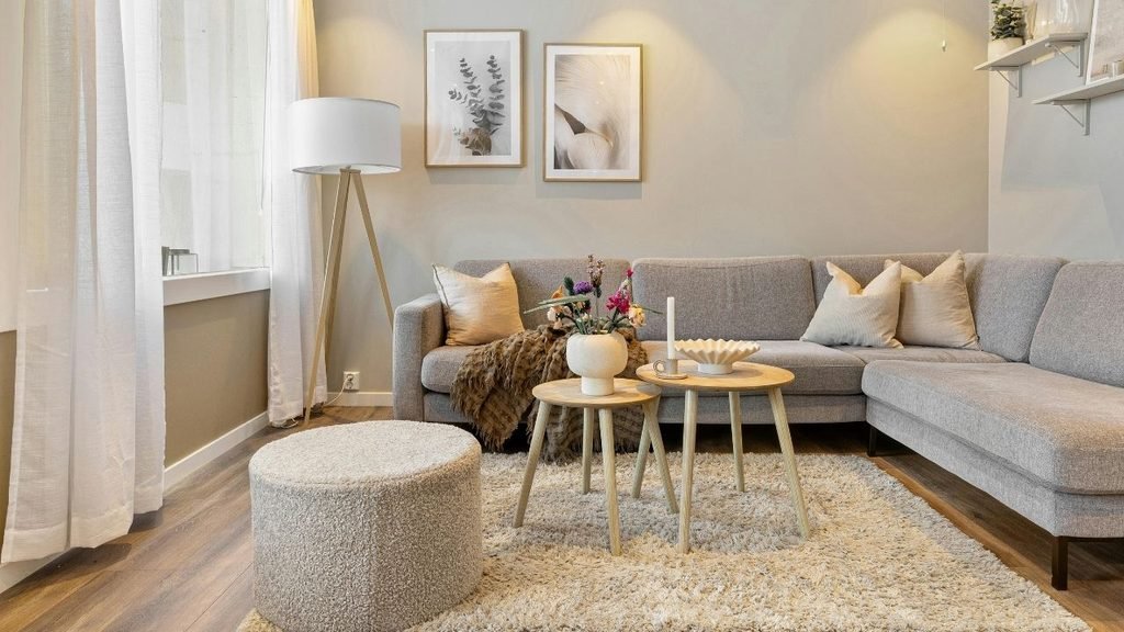 Cozy living room with a gray sectional sofa, shaggy cream rug, round wooden side tables, and framed nature prints