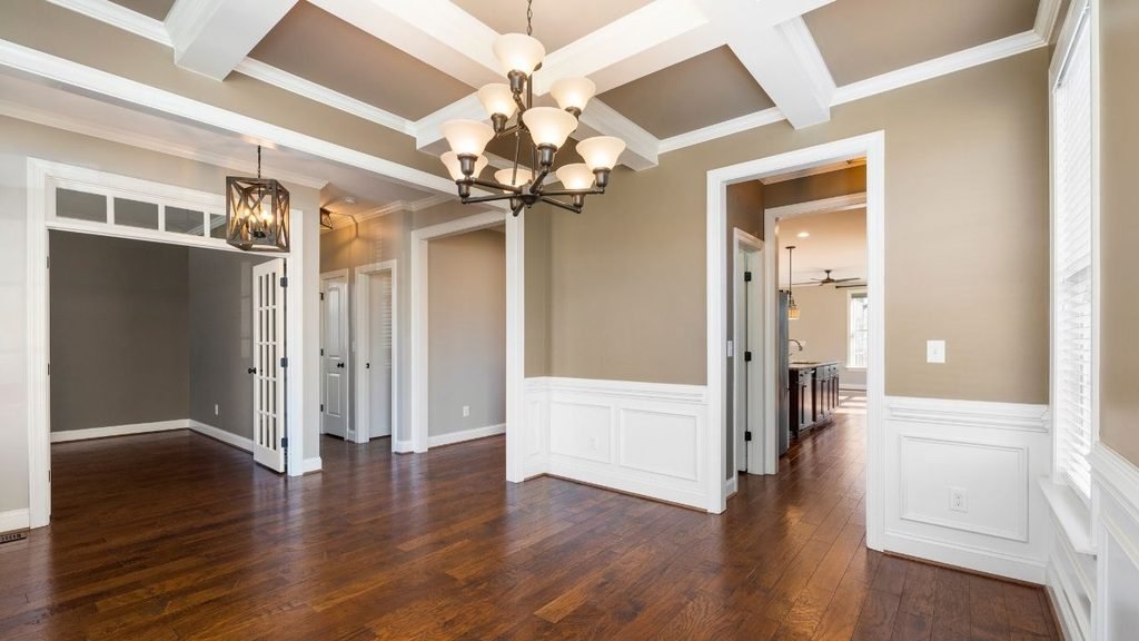 Empty dining room with a coffered ceiling, bronze chandelier, wainscoting, and dark hardwood floors