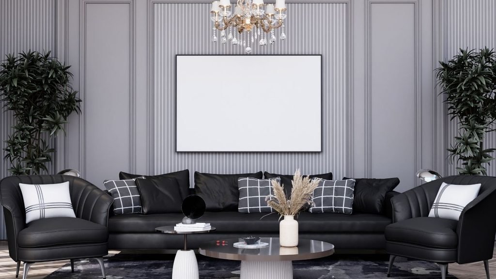 Elegant living room with black leather sofa and armchairs, a crystal chandelier, and a large blank frame on paneled gray walls