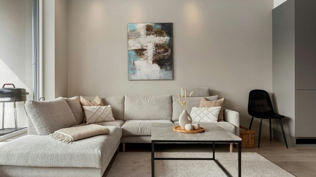 Modern neutral living room with a beige sectional sofa, marble coffee table, black accent chair, and abstract wall art