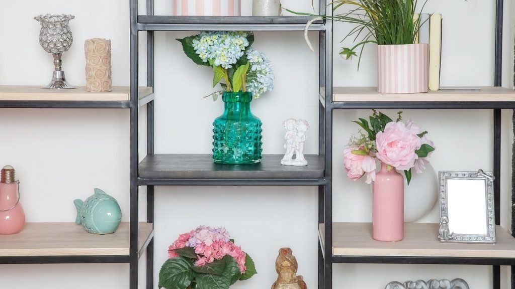 Black metal shelving unit styled with pastel decor, including teal and pink glass vases, fresh flowers, and small ornaments