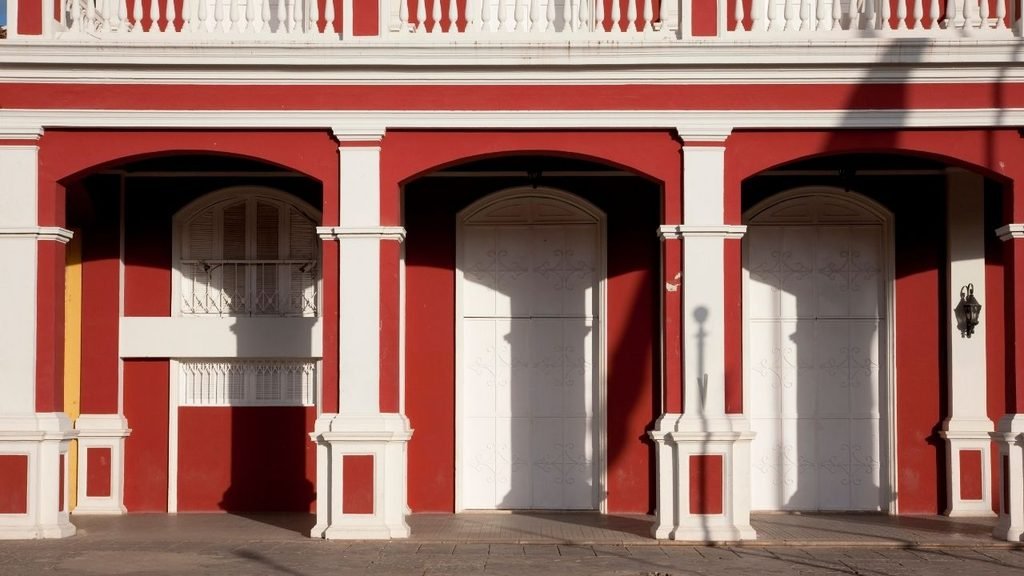 Red and white colonial building facade with arched doorways, shuttered windows, and a balustraded upper balcony