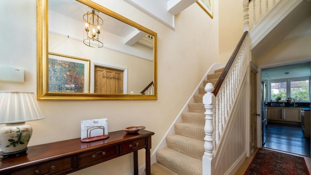 Traditional entryway with a gold-framed mirror, console table, chandelier, and carpeted staircase with white balusters