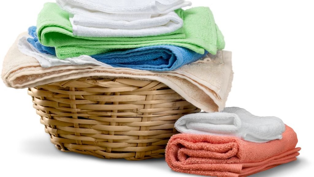 Assorted folded towels in green, blue, white, and coral stacked in and beside a wicker basket
