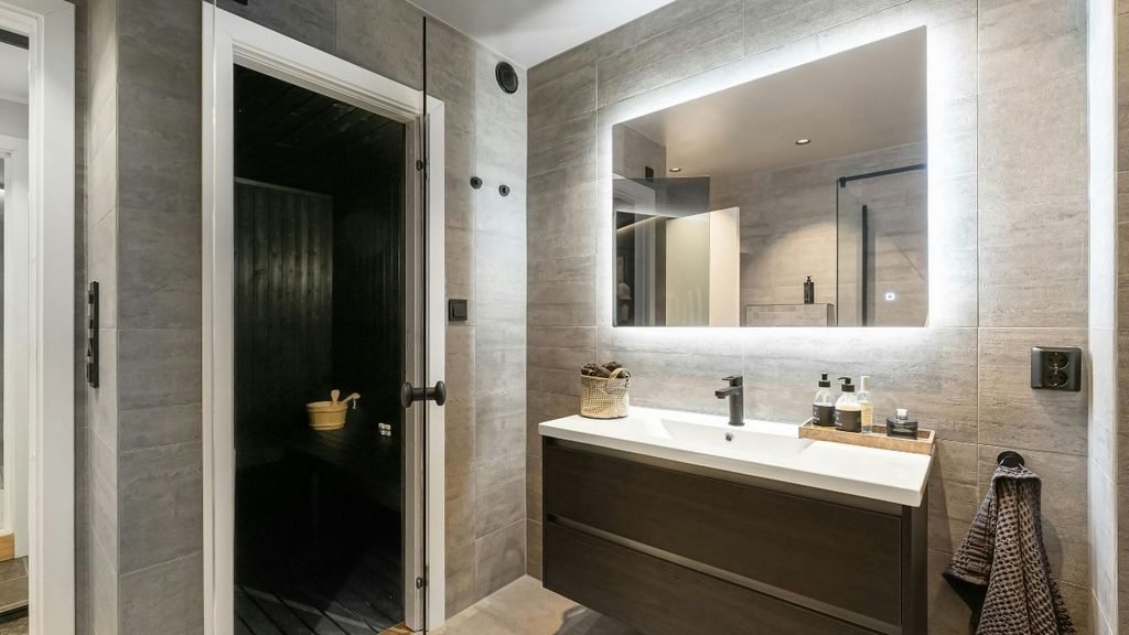 Modern bathroom with a large backlit LED mirror above a floating vanity, creating the illusion of a bigger room
