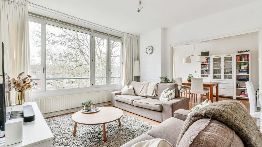 Cozy Scandinavian-style living room with neutral sofas, round wood coffee table, shag rug, and large window overlooking bare trees