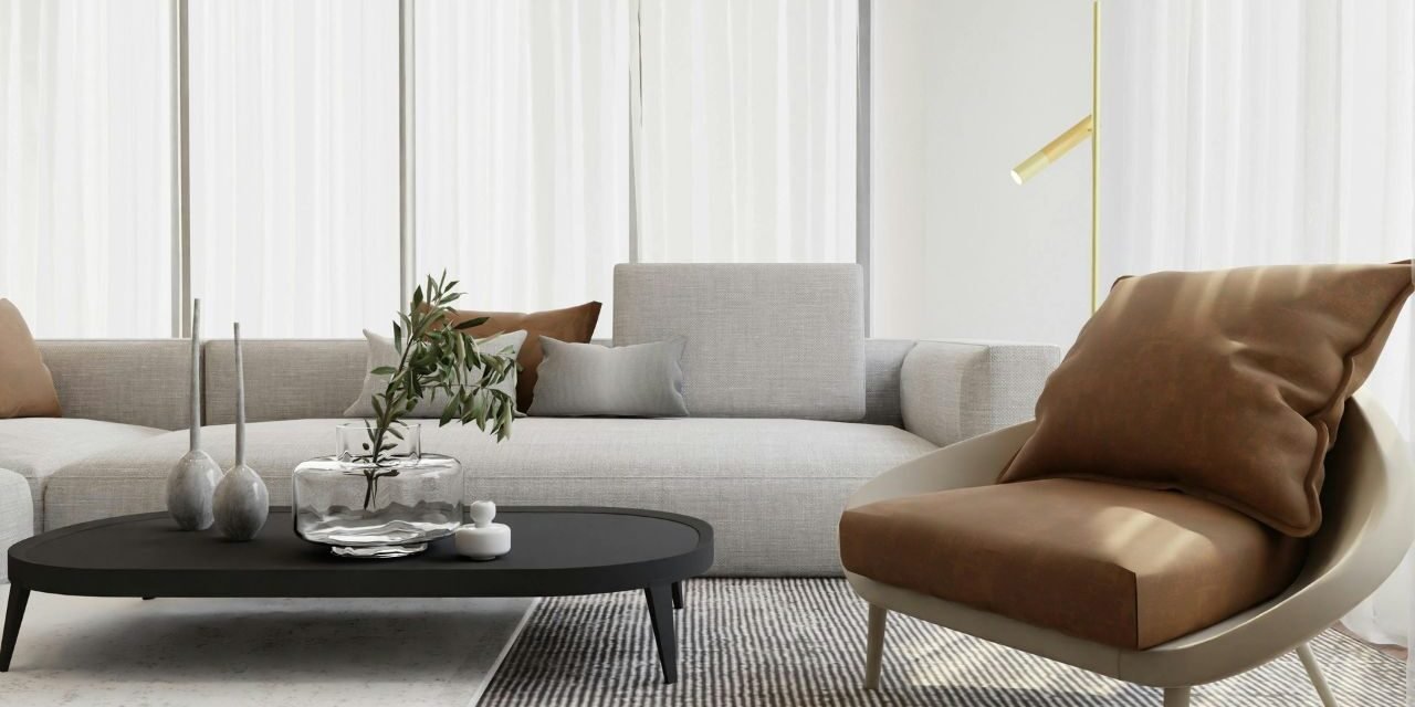 Living room with sheer curtains, a glass vase on a black coffee table, and a tan leather accent chair beside a slim gold floor lamp