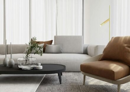 Living room with sheer curtains, a glass vase on a black coffee table, and a tan leather accent chair beside a slim gold floor lamp