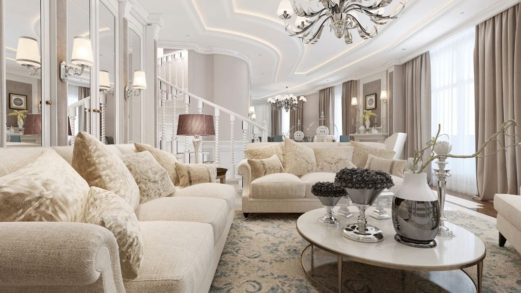 Luxurious cream living room with crystal chandelier, curved staircase, mirrored walls, and plush beige sofas with patterned area rug