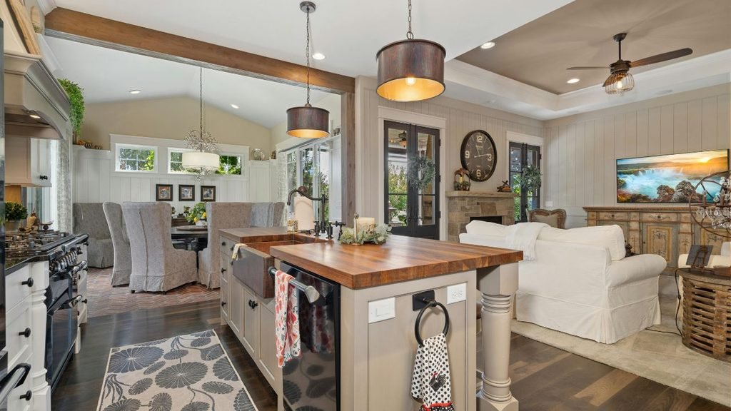 Open concept interior featuring a modern farmhouse kitchen with a wood-top island and copper sink overlooking a cozy living room and dining area.