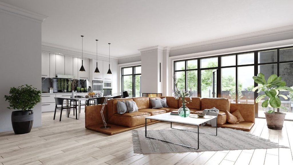 Open-concept living room with tan leather sectional sofa, marble coffee table, fringed area rug, and adjoining modern white kitchen