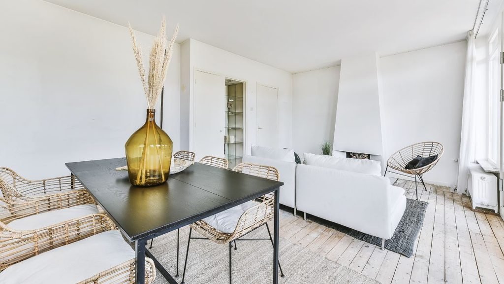 Open-plan dining and living area with a black table, rattan chairs, and a rug used to visually separate the seating zone from the dining zone