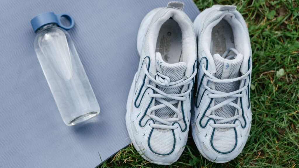 Pair of white and blue sneakers next to a glass water bottle on a gray yoga mat, ready to store on a shoe rack organizer after a workout