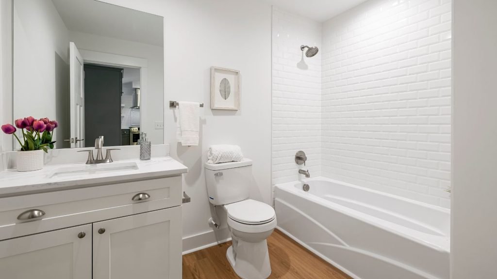 Small white bathroom with subway tile shower-tub combo, floating vanity, and wood-look flooring