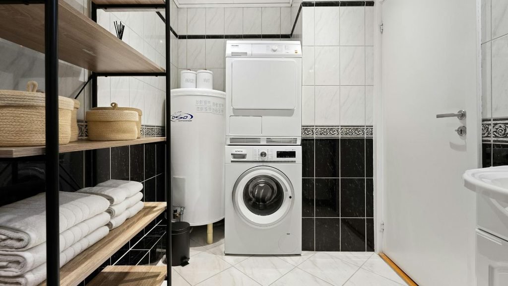 Small laundry room with stacked washer and dryer, water heater, and wood storage shelving with baskets