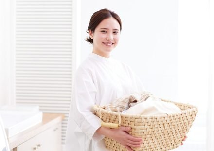 Smiling woman in white blouse holding a wicker laundry basket filled with clean clothes