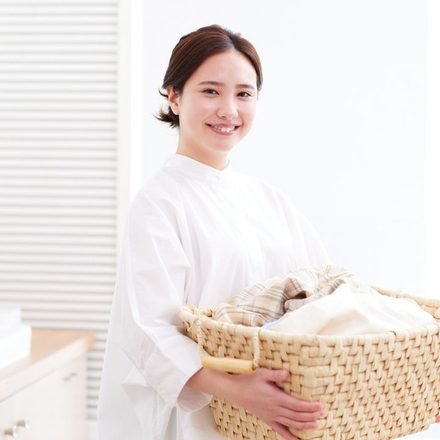 Smiling woman in white blouse holding a wicker laundry basket filled with clean clothes