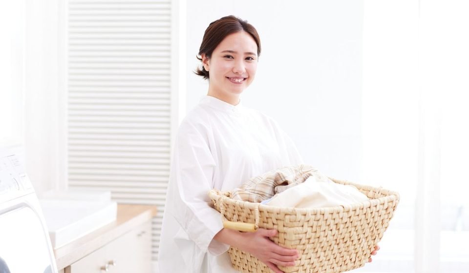 Smiling woman in white blouse holding a wicker laundry basket filled with clean clothes