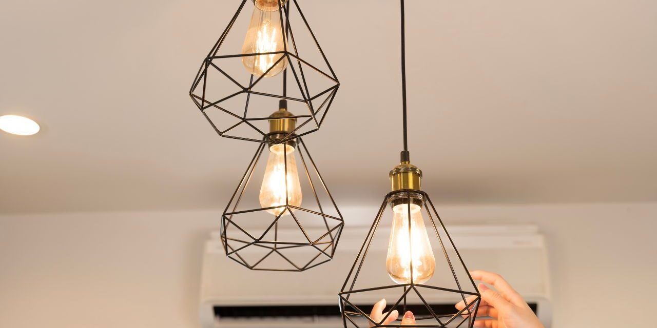 Soft glow light bulbs in black geometric cage pendant fixtures above a bedroom nightstand area