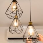 Soft glow light bulbs in black geometric cage pendant fixtures above a bedroom nightstand area