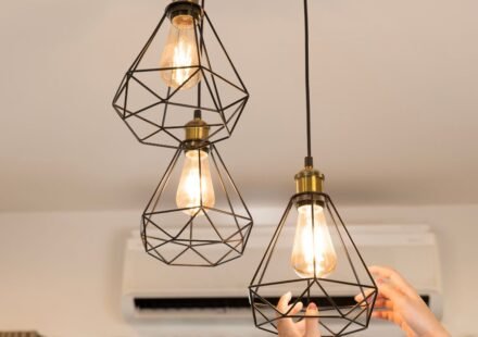 Soft glow light bulbs in black geometric cage pendant fixtures above a bedroom nightstand area