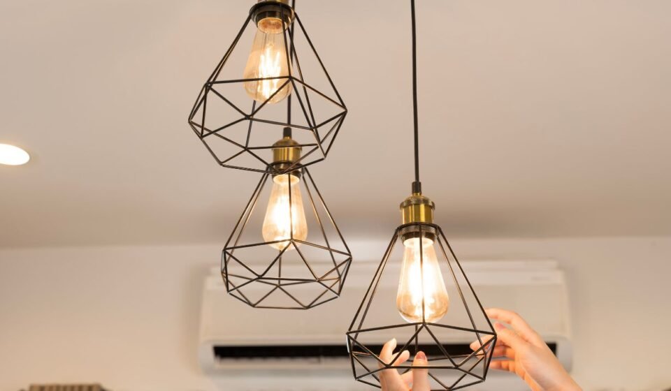 Soft glow light bulbs in black geometric cage pendant fixtures above a bedroom nightstand area