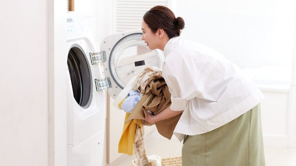 Woman bending down to load an armful of clothes into a front-load washing machine