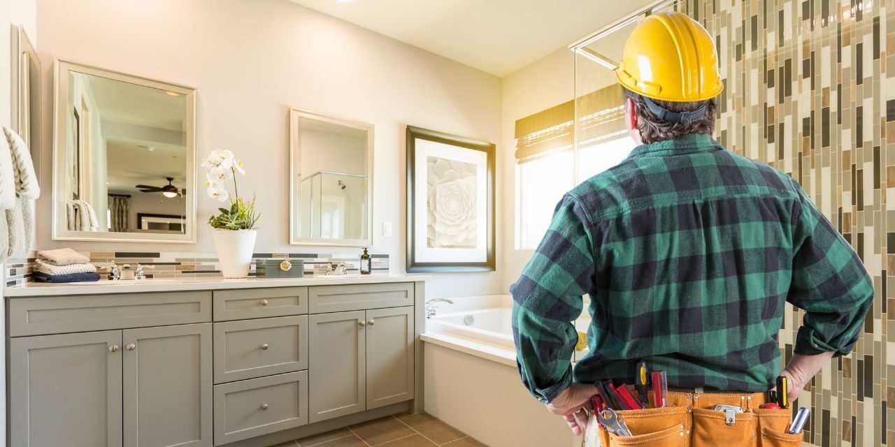 Contractor in a hard hat reviewing a finished bathroom with a gray vanity and mosaic tile shower wall