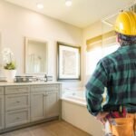 Contractor in a hard hat reviewing a finished bathroom with a gray vanity and mosaic tile shower wall