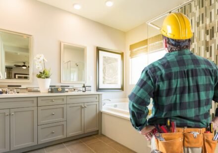 Contractor in a hard hat reviewing a finished bathroom with a gray vanity and mosaic tile shower wall