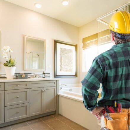 Contractor in a hard hat reviewing a finished bathroom with a gray vanity and mosaic tile shower wall