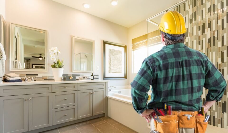Contractor in a hard hat reviewing a finished bathroom with a gray vanity and mosaic tile shower wall