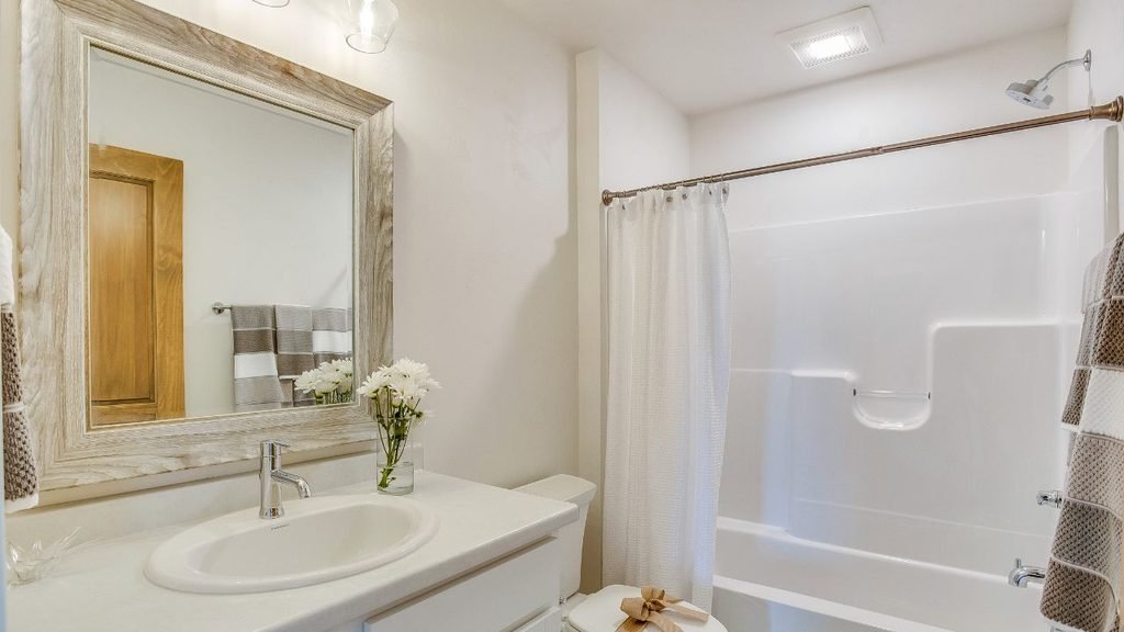 Budget-friendly bathroom update with a shower-tub combo, white vanity and a weathered wood-look mirror, a cheap remodel option