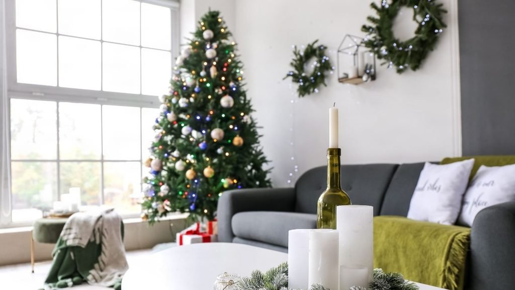 Christmas living room wall decor with lit wreaths above a grey sofa and a tree with colorful lights by a sunny window