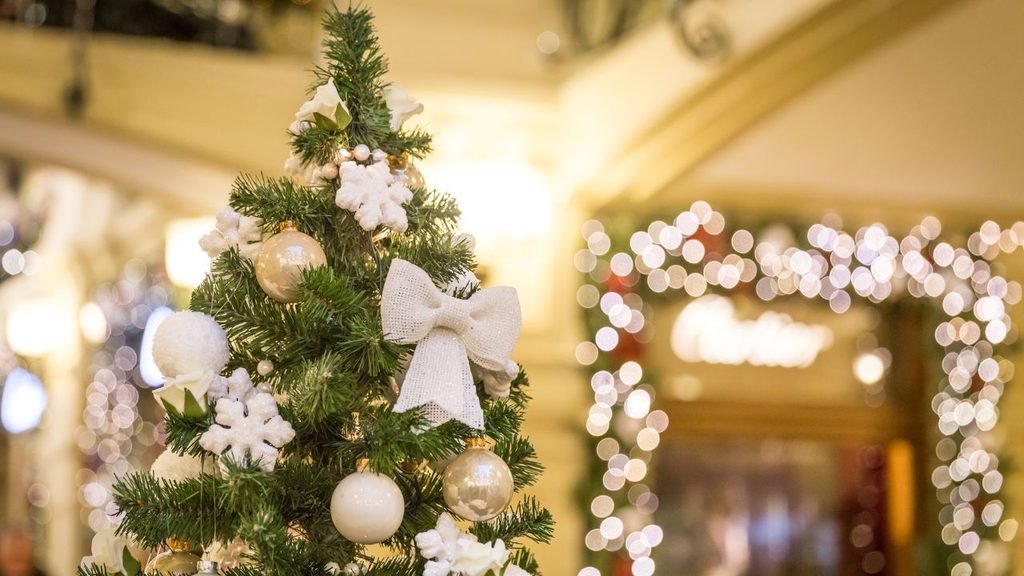 Compact Christmas tree with white ornaments, snowflakes and a burlap bow, a charming christmas tree design idea for small spaces