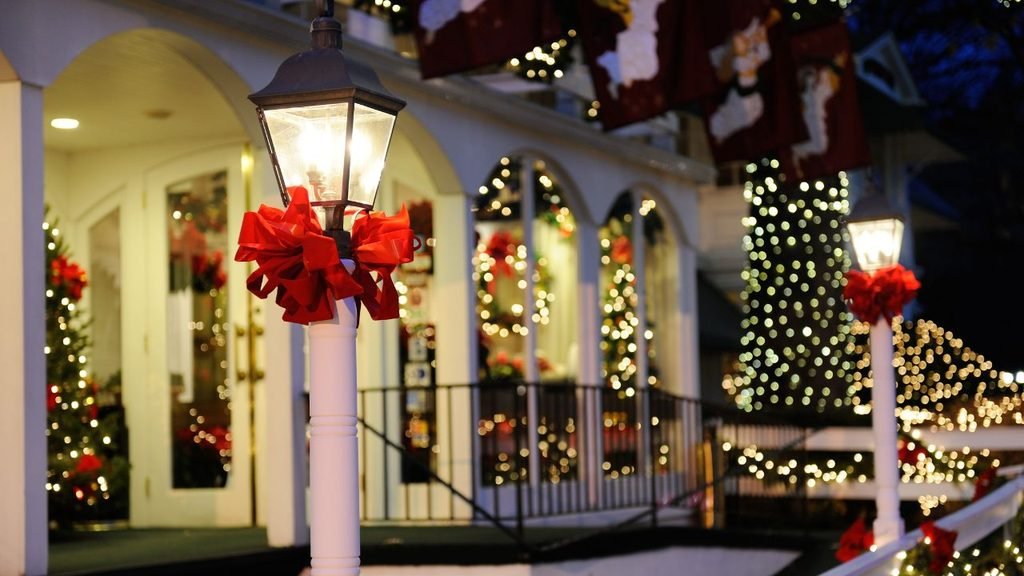 Festive porch with a lamp post tied with a big red bow and Christmas trees glowing with string lights at dusk