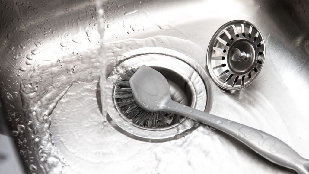 Running water and a scrub brush in a stainless steel kitchen sink drain, a simple cleaning hack for the kitchen