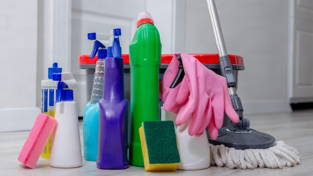 Collection of spray bottles, sponges, pink rubber gloves and a mop, essential supplies for cleaning small spaces